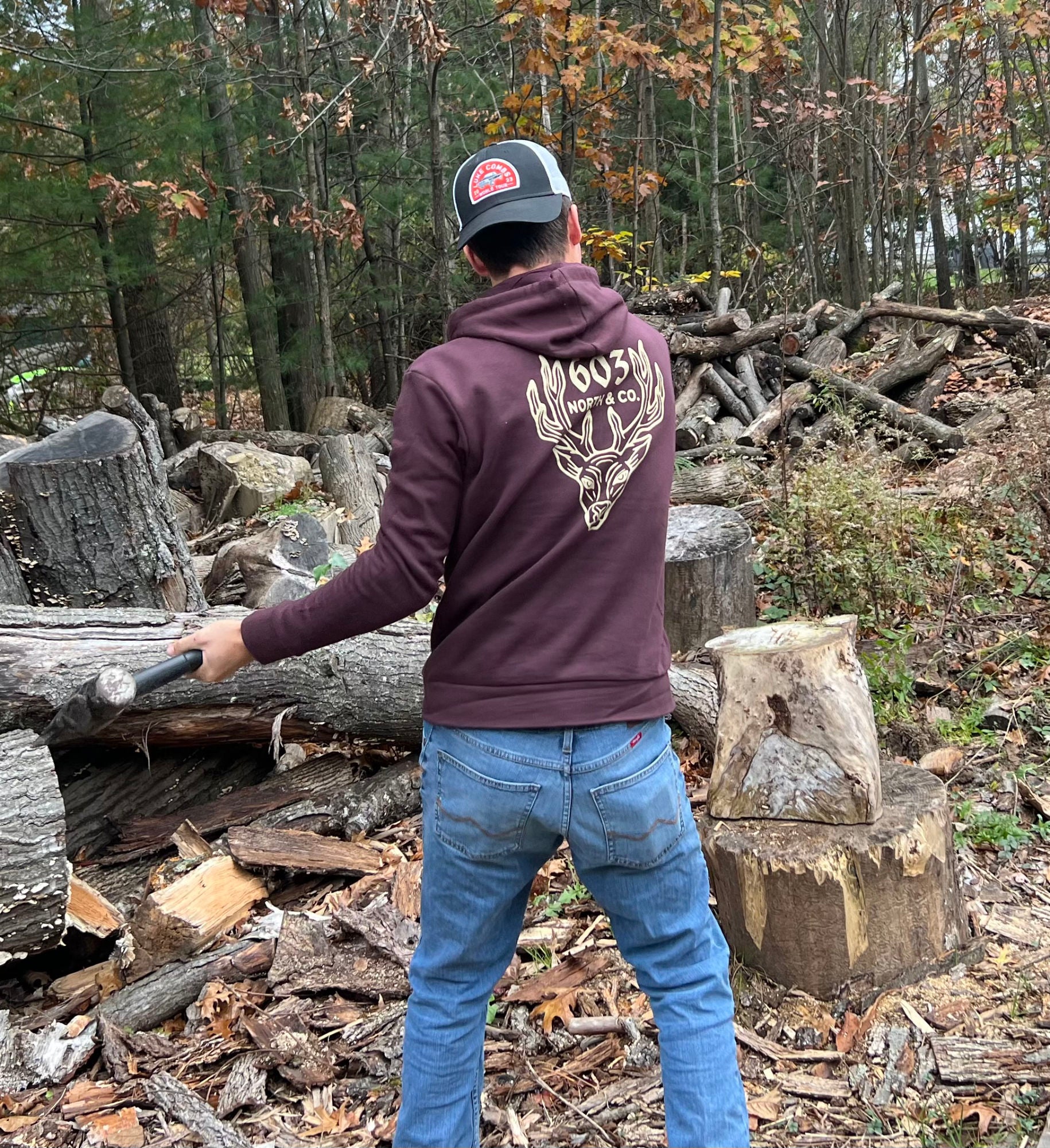 Swinging a hammer wearing the an oxblood-colored hoodie with a large deer design printed on the back.